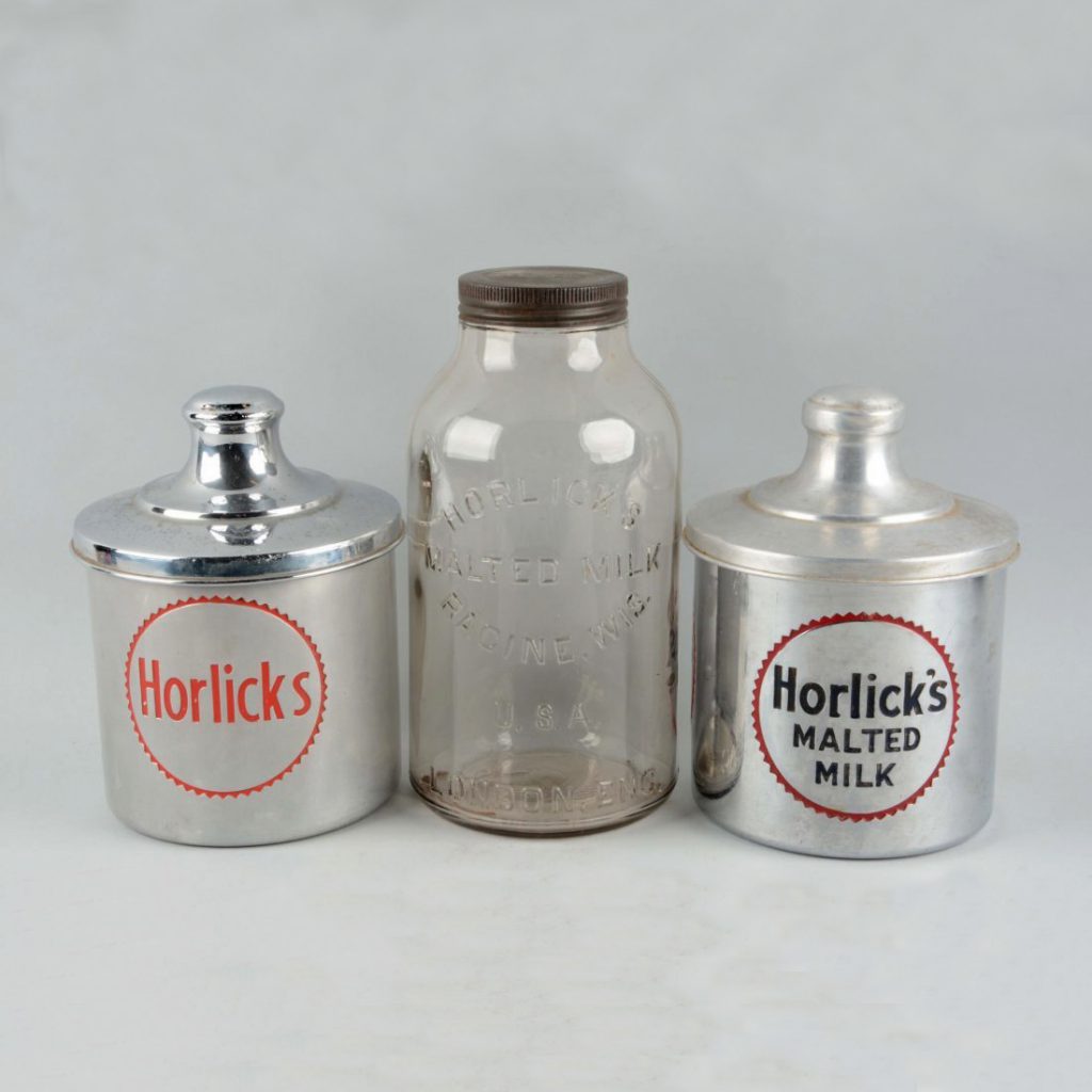 A photograph of three containers, two made of metal, and one a glass jar. They're all labeled "Horlick's"