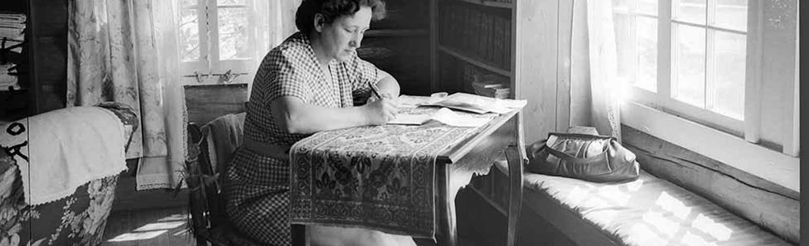 A woman sits writing at a desk