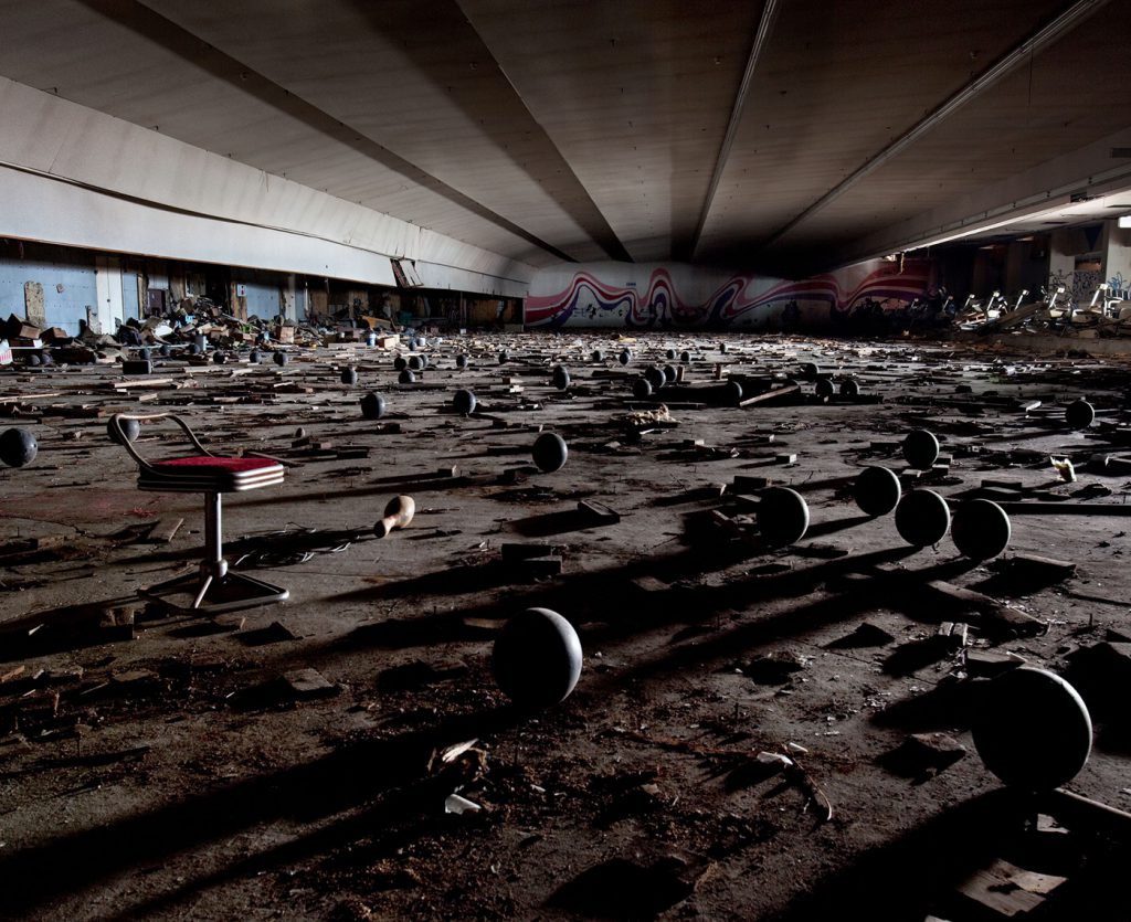 Photograph of an abandoned bowling hall with bowling balls and other debris strewn across the floor.