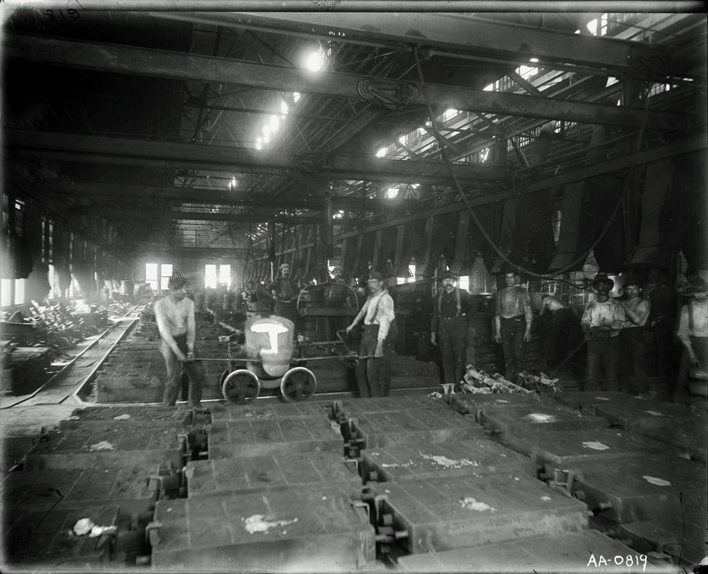A black and white image of the shop floor of a factory showing workers posing with machines.