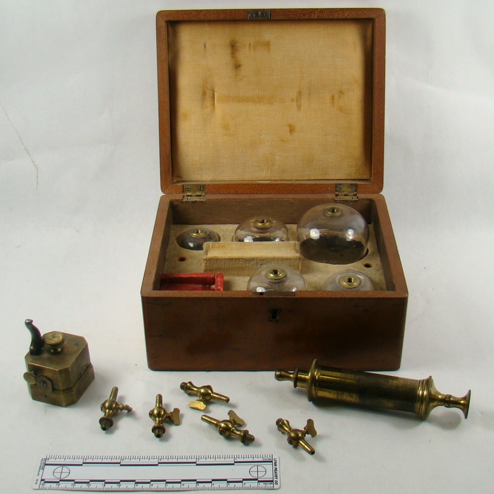Image of a wooden box with several glass bells of different sizes within. A brass hose with different nozzle sizes sits beside it.