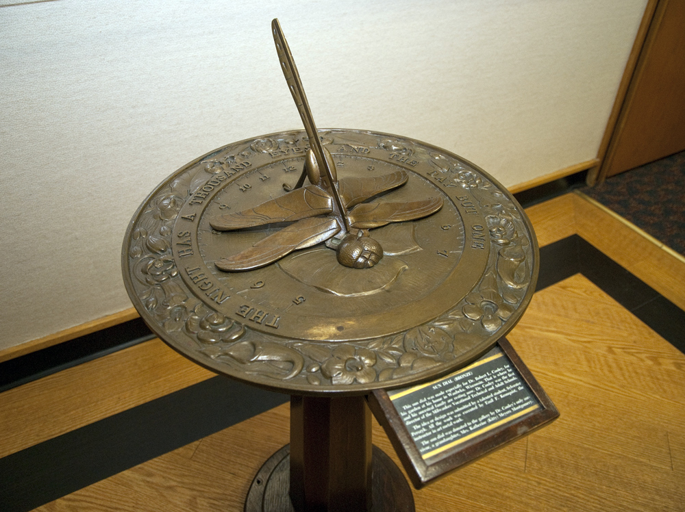a broze sundial with a dragon fly tail as the shadow-caster.