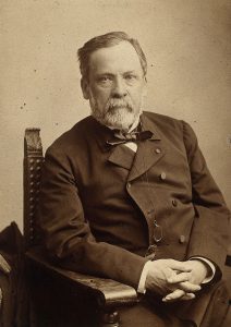 A portrait of Louis Pasteur with hands folded looking at the viewer
