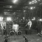 A black and white image of the shop floor of a factory showing workers posing with machines