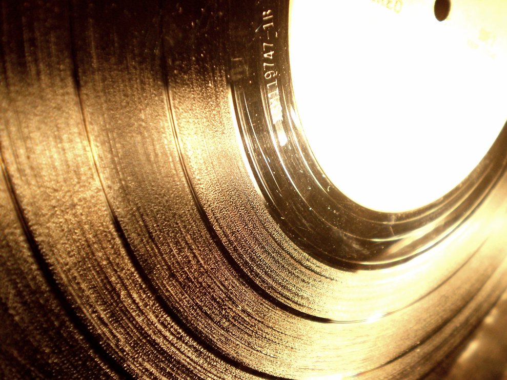 A close-up of a black vinyl record showing the grooves which create the sound