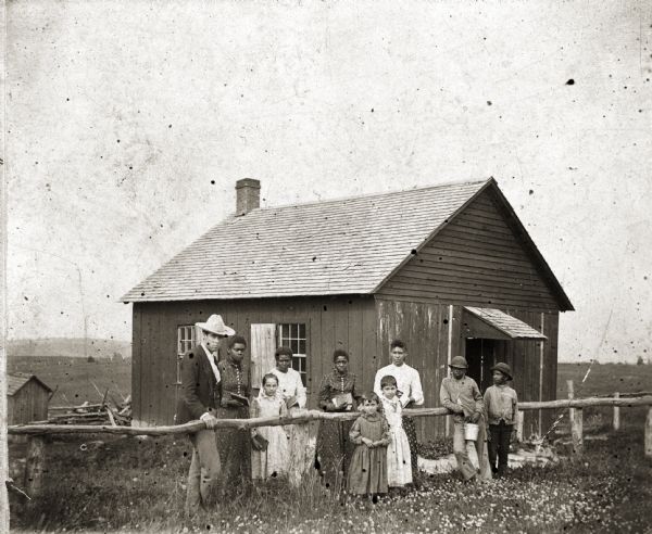 a black and white photo of the Pleasant Ridge schoolhouse showing several school children and two adults in front of the one room building