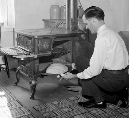 A black and white photo of a man putting a pasty in a wood stove