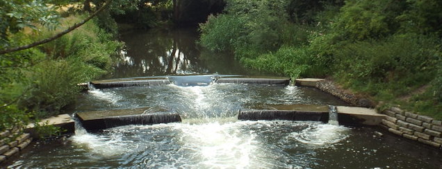 A color photo of a small stone weir across a tiny river