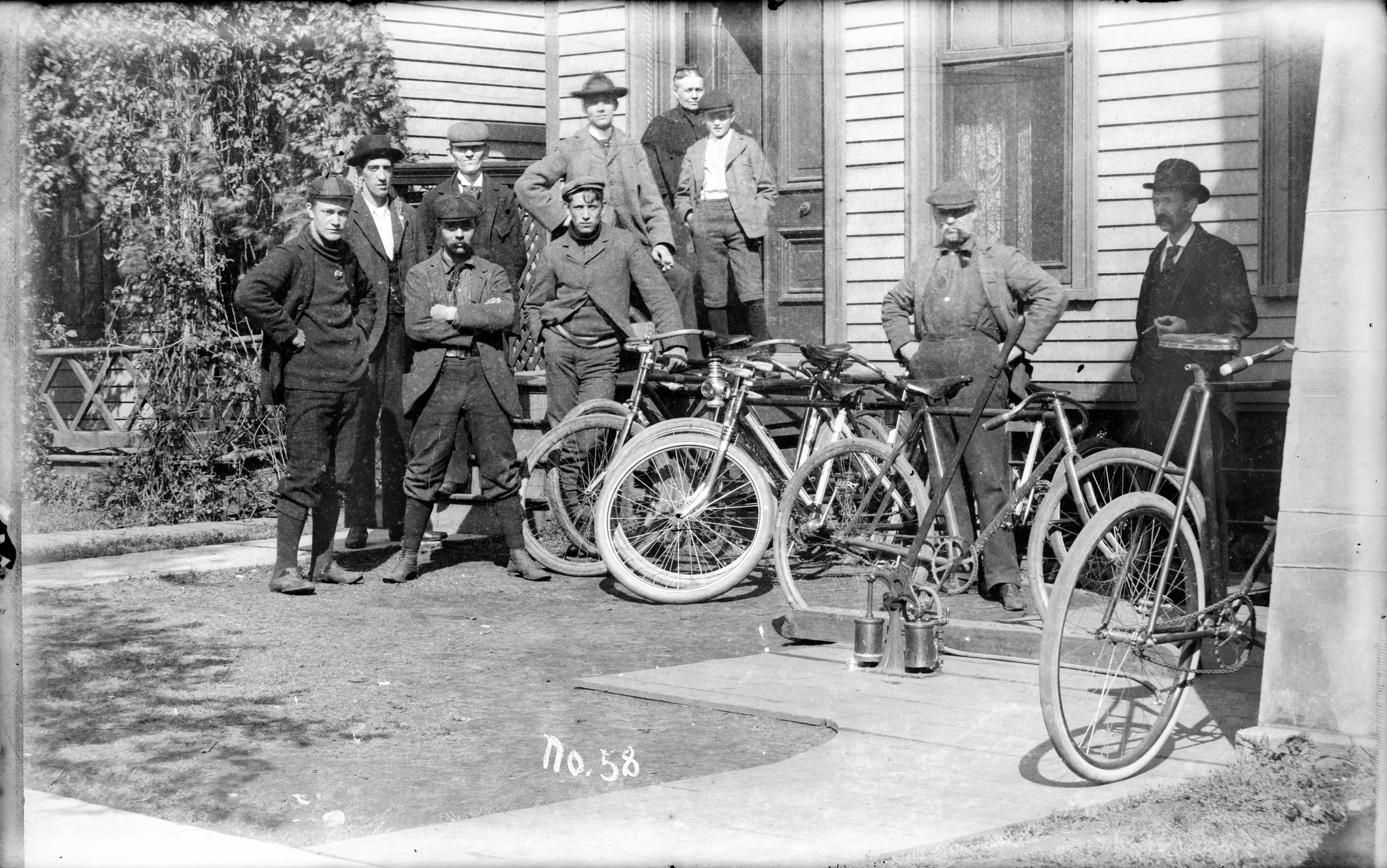 A group of men post with their bikes beside a house