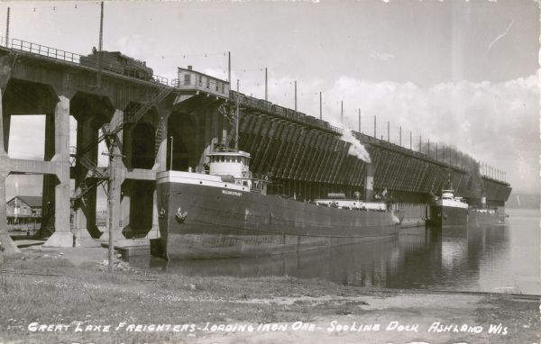 a train on a large dock over a ship, dumping ore into the hold of the ship.