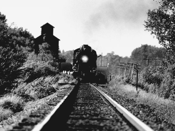 a black and white photo of an engine on the tracks and a conductor waving from the window
