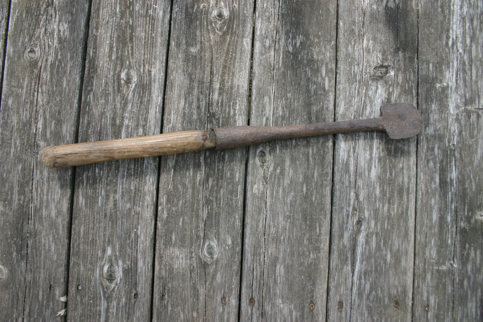a color photograph of a metal tool with a rounded edge and a wooden handle about two feet long