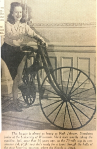 a young woman sits on the wooden bike and smiles at the camera.