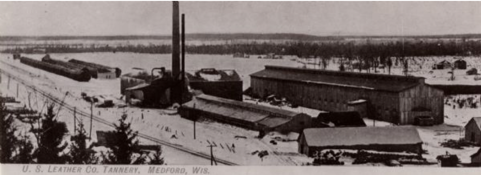 A black and white photo of a long low building with a tall smoke stack