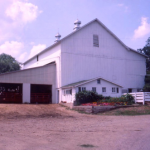 a color photo showing a swiss style bank barn painted white with a lean-to on one side