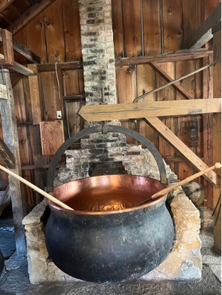 Copper cheese kettle, blackened on the exterior, cauldron-like with steel handle. Photographed above a traditional stove.