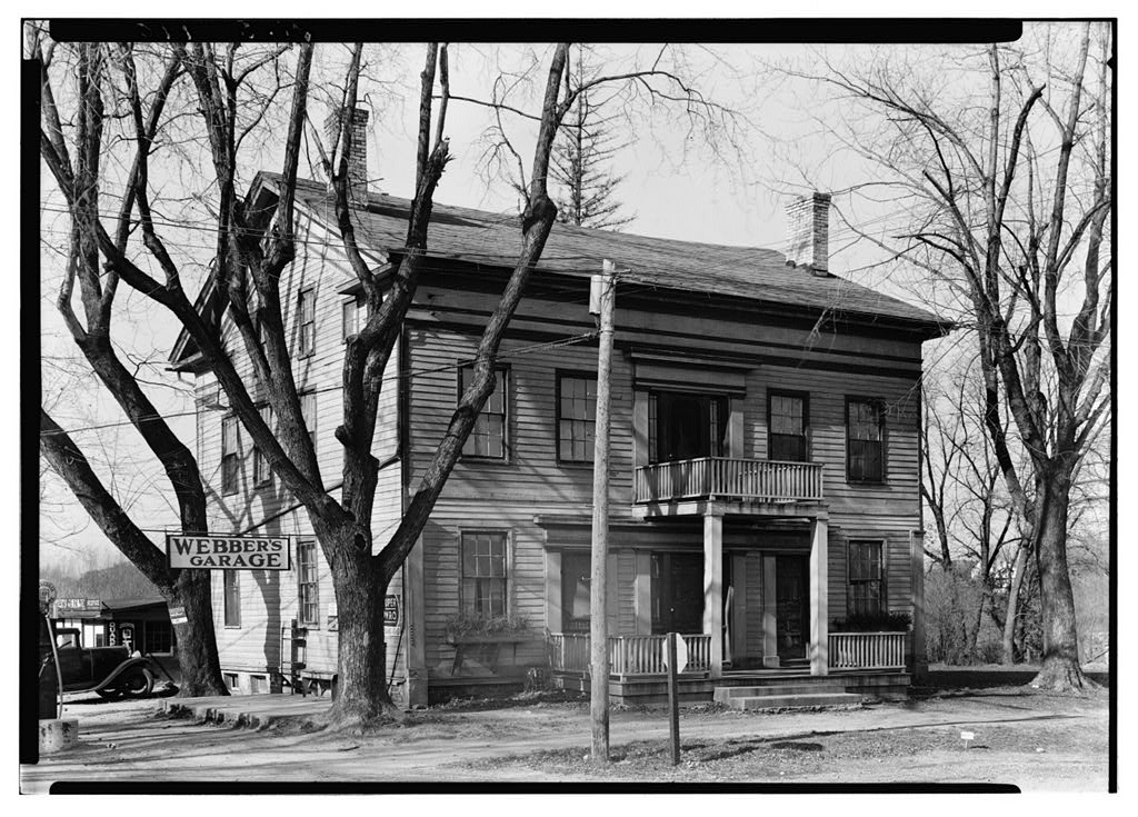 Black and white photograph of a two-and-a-half story building with small porch around the central entrance. A sign extending from the side of the building reads, "Webber's Garage."