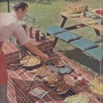 Detail from a Better Homes and Gardens photoshoot showing a man at an outdoor barbecue with steaks and corn on a grill as well as a cast iron pan with potatoes