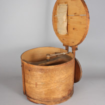 A wooden drum with open lid revealing interior mechanism