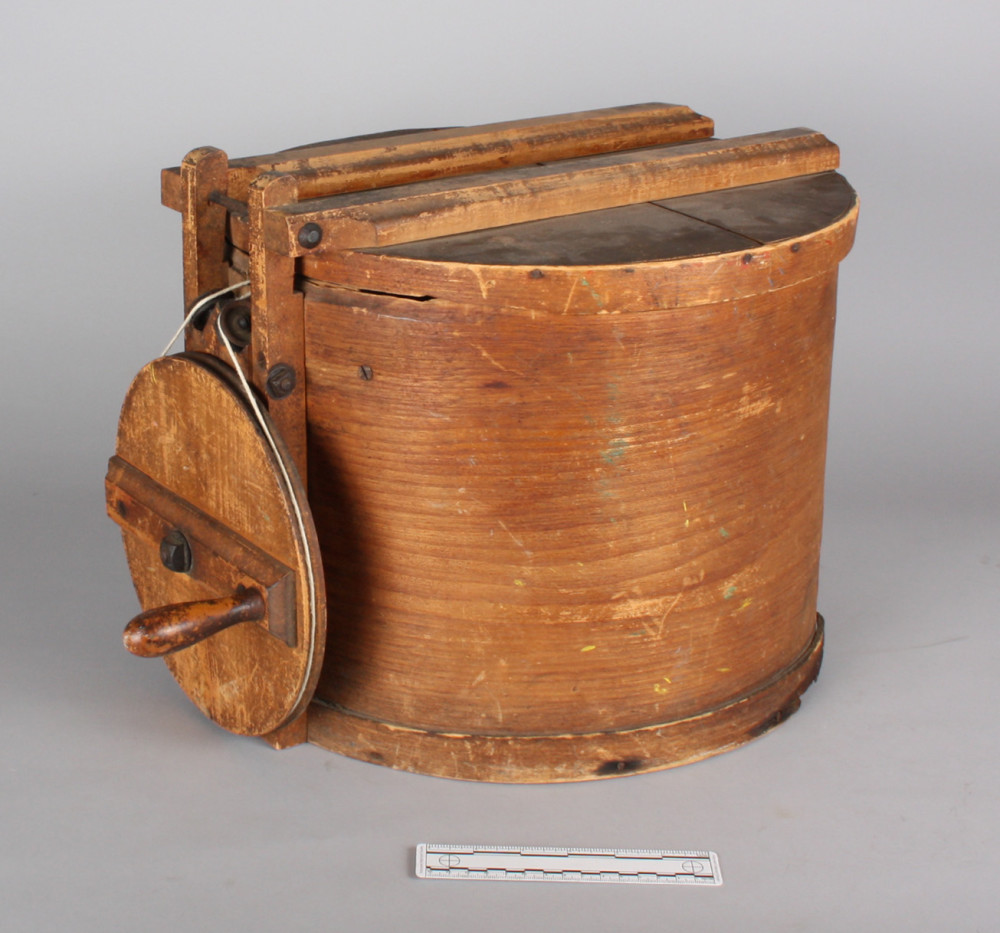 A wooden drum with lid and crank wheel.