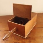 A wooden ballot box, with a small handle, a hinged lid, and a hole to insert a marble.