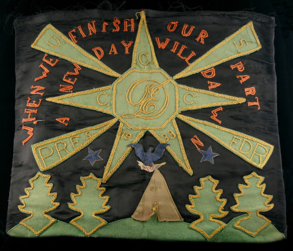 A black pillowcase with embroidery and applique, featuring a CCC emblem, an eagle over a tent, applique trees, and embroidered text, “When we finish our part a new day will dawn.”