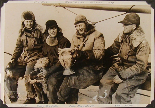 Photograph of four men sitting on a boat holding a trophy.