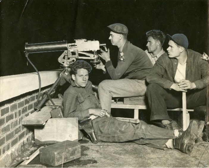 Four young men sit on a rooftop guarding a building.