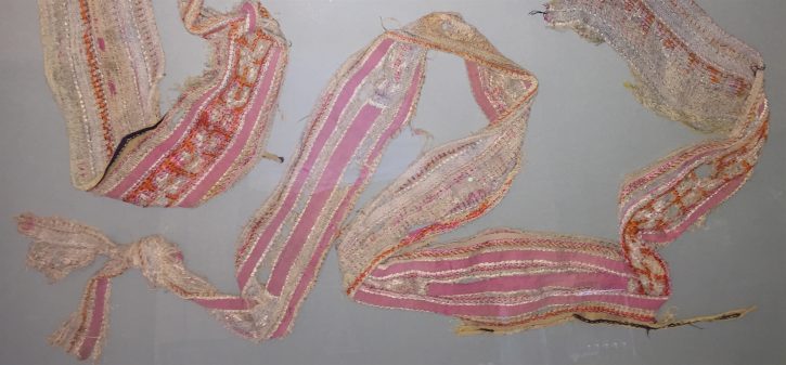 A detailed image of a pink and cream colored, woven and embroidered baby sash.