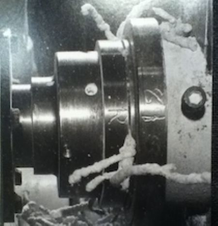 A close-up photograph of an industrial extruder, puffs of corn feed byproduct leak from the side.