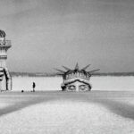 A black-and-white photograph of the head and torch-in-hand of the statue of liberty on a frozen lake.