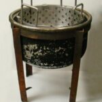 A metal pot on four metal legs inside of which sits a colander-like pan.