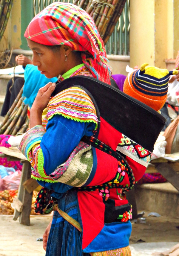 A woman wearing a baby sash and carrier in a market.