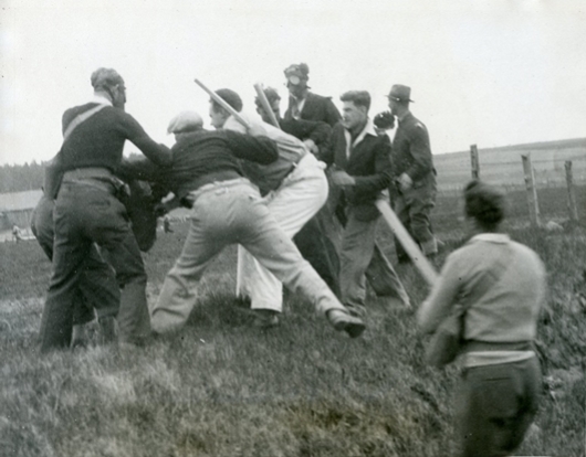 A scene of unrest as men, some armed with night stucks, one wearing a gas mask, fight along a fence line.