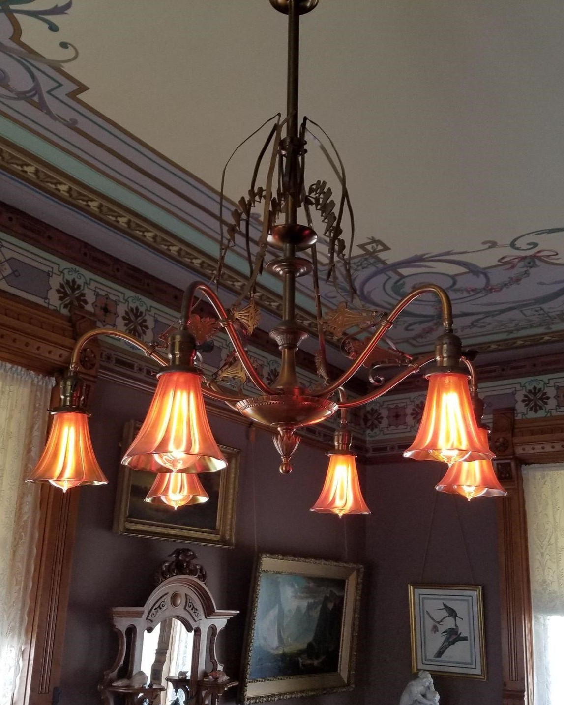 Photograph of an ornate brass changelier with six lights and glass diffusers.