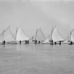 A black and white photograph if five ice boats on a frozen lake.