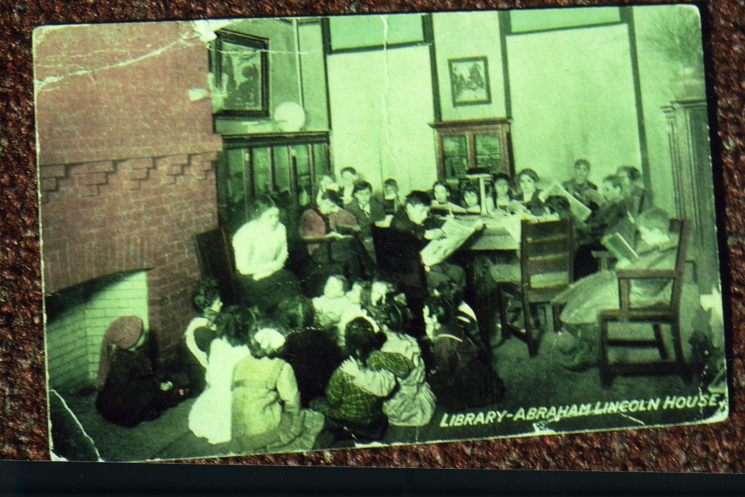 Colorized postcard of the interior of the library at the Lincoln House. Children gather around as a woman tells a story.