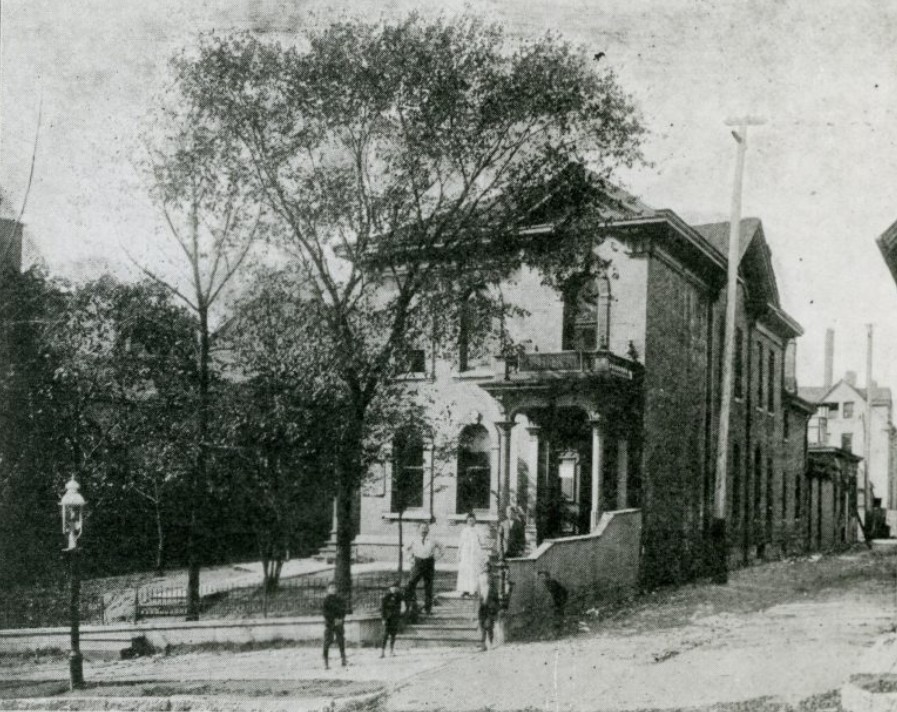 A black-and-white photograph of the second Settlement House. Two men, a woman, and three children pose in front of the building.