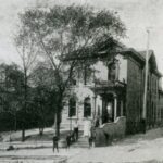 A black-and-white photograph of the second Settlement House. Two men, a woman, and three children pose in front of the building.