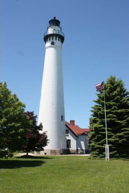 Photograph of the Wind Point Lighthouse and keepers house. The lighthouse towers over the house. The tower, constructed of brick, stuccoed, and painted white, is round and has an observation deck that encircles the lantern.
