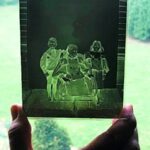 A hand holds a glass plate negative up to the light revealing the negative image of a seated women posed with children.