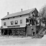 A black-and-white photograph of a wooden building with porch.