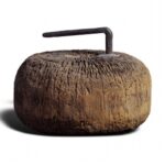 A rounded wooden block with a iron handle protruding from the top.