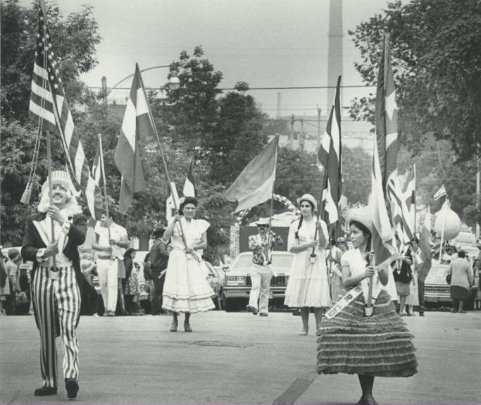 Three girls and a man dressed in traditional costumes carry flags and lead a parade for Fiesta Mexicana.