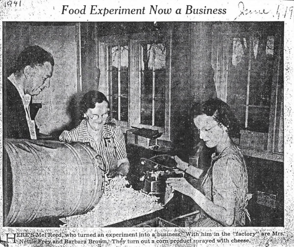 A newspaper clipping of a man overseeing two women create corn puff snacks in a private home.