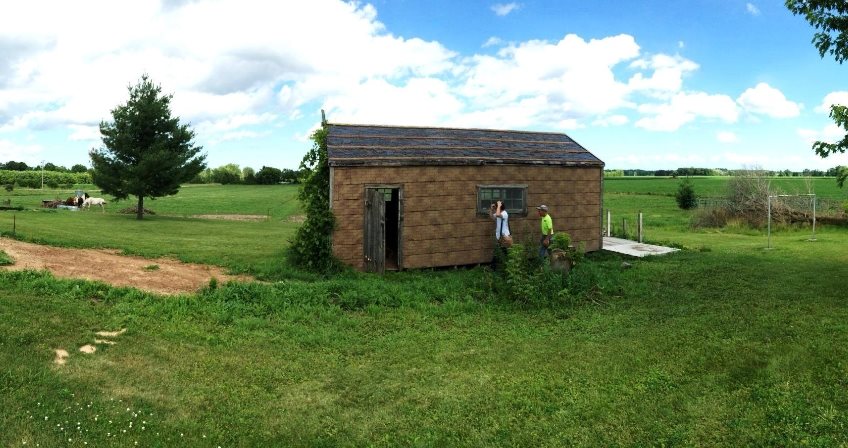 A small wood frame building with small windows and asphalt siding.