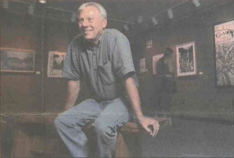 A man sits on a bench in a gallery space.