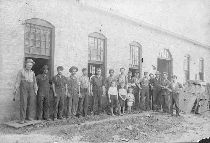 A group of men posed in front of a workshop.