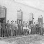 A group of men posed in front of a workshop.