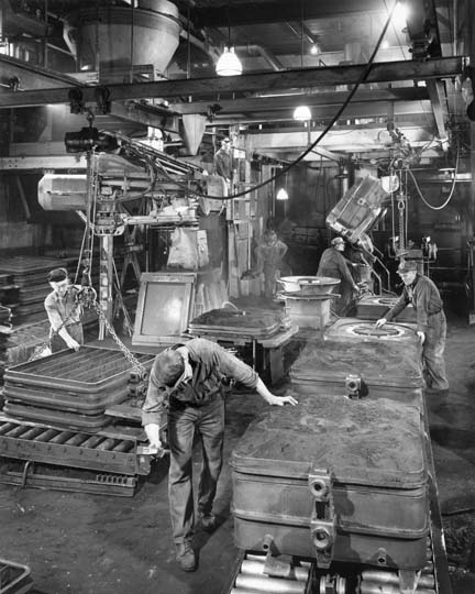 Interior photograph of the foundry showing an assembly line of men preparing casting molds.